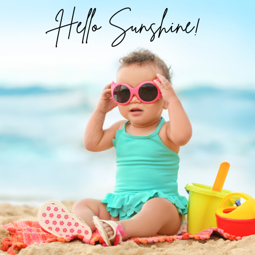 toddler sitting on a beach blanket putting on pink sunglasses.