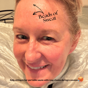 Kelly sitting in her portable sauna with rosy cheeks and beads of sweat on her forehead during a session.