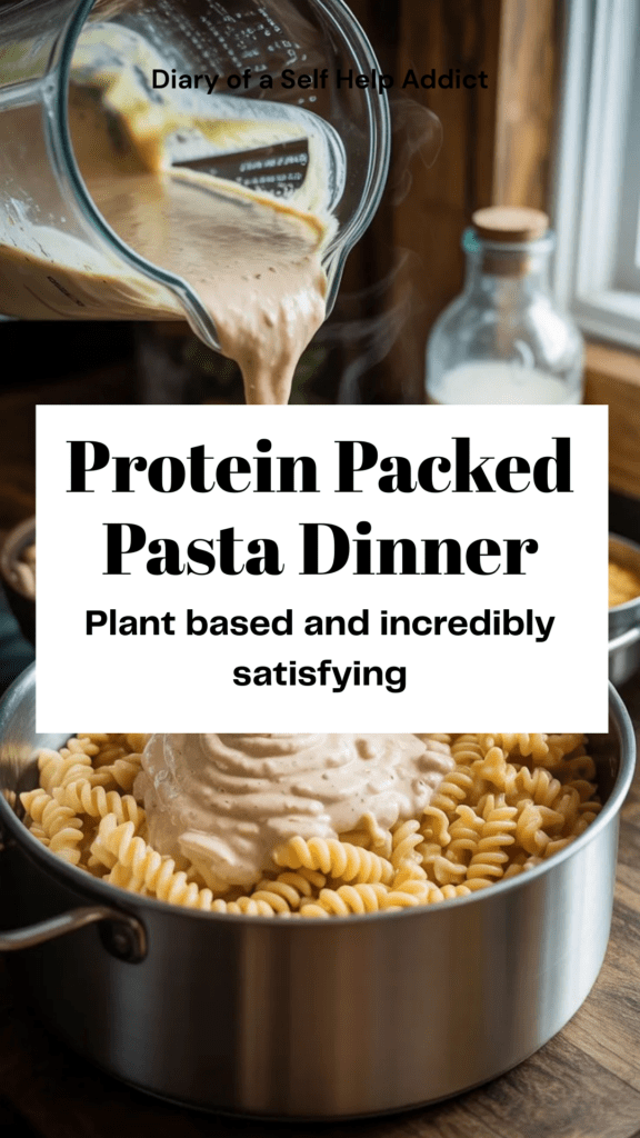 Blender pouring creamy white bean Alfredo sauce over chickpea pasta in a pot. Ingredients (beans, soy milk, nutritional yeast) sitting beside the blender.