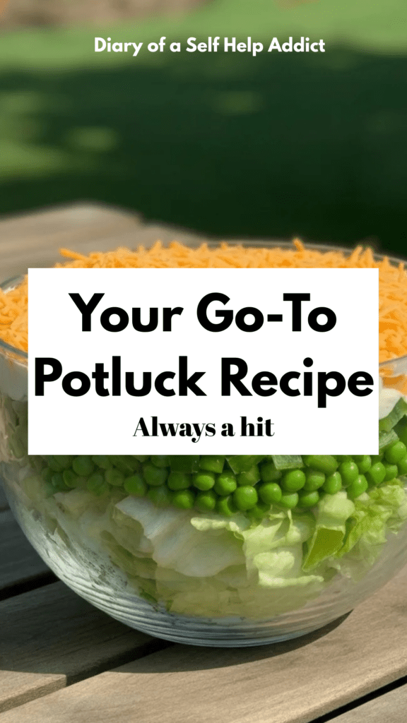 A large clear glass bowl filled with a layered salad, each vibrant layer visible—crisp iceberg lettuce, green peas, chopped celery, peppers, creamy dressing, and shredded cheddar on top, set on a sunlit outdoor picnic table.