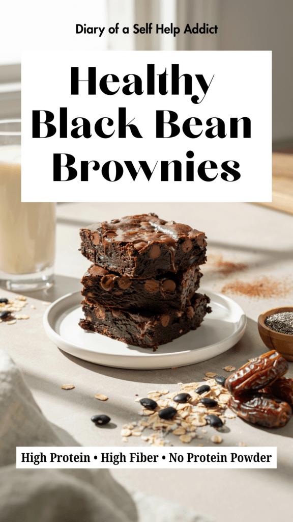A stack of three fudgy black bean brownies on a white ceramic plate with melted dark chocolate chips on top. A glass of soy milk sits in the background with scattered cocoa powder, rolled oats, black beans, Medjool dates, and a small bowl of chia seeds. Bright natural kitchen lighting creates a cozy, healthy baking feel.