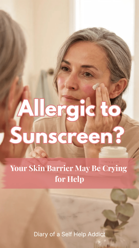 Close-up of a woman in her early 50s gently applying mineral sunscreen to one side of her face while examining slight redness in the mirror. Bright natural lighting, healthy glowing skin, calm bathroom setting, realistic photography style with a focus on skincare and sensitive skin.