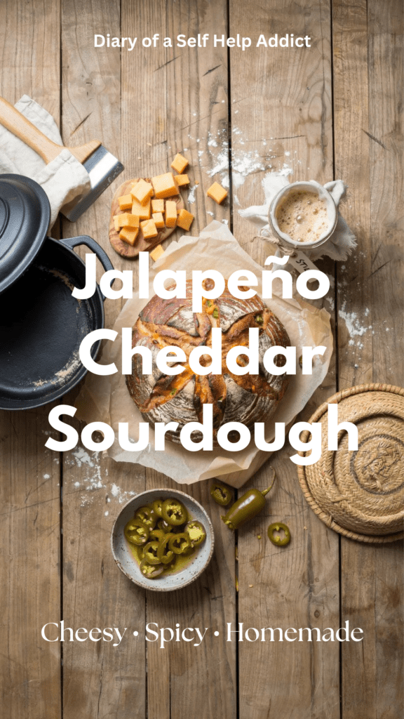 A rustic, golden-brown round loaf of jalapeño cheddar sourdough sitting on a wooden cutting board, with a few slices of creamy cheddar and fresh/pickled jalapeño peppers scattered around it. The crust is deeply browned and artisan-looking, with a beautiful scored design across the top. Warm, natural kitchen lighting and a cozy homemade-baking aesthetic.