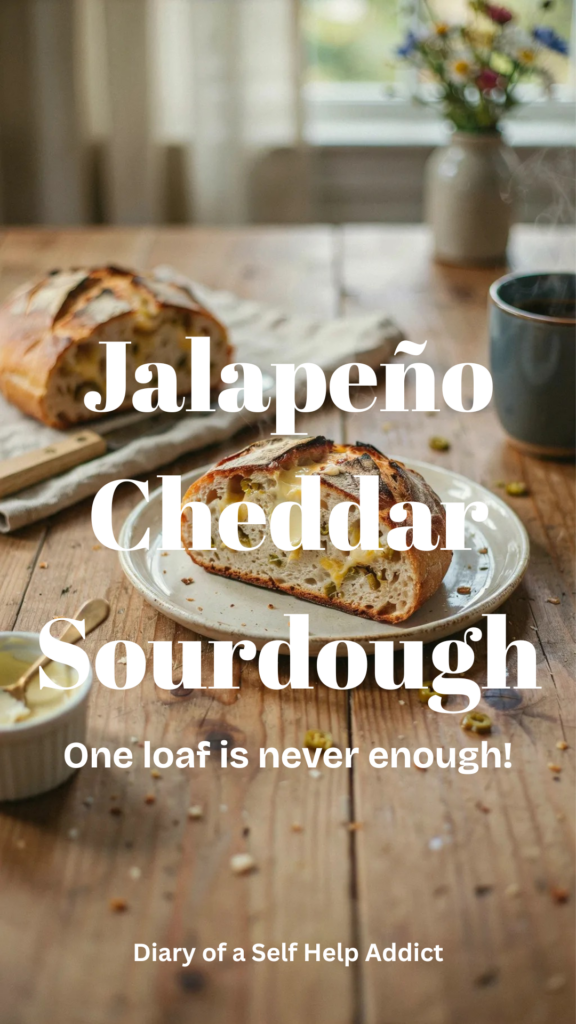 One thick slice of jalapeño cheddar sourdough spread generously with butter, sitting on a rustic plate beside the remaining loaf. The butter is beginning to melt into the warm, chewy crumb, highlighting the cheese and jalapeño throughout the bread. Cozy breakfast or brunch atmosphere.