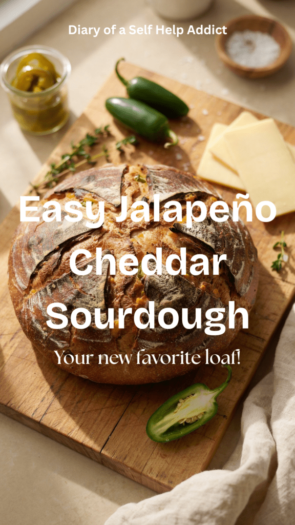 A rustic, golden-brown round loaf of jalapeño cheddar sourdough sitting on a wooden cutting board, with a few slices of creamy cheddar and fresh/pickled jalapeño peppers scattered around it. The crust is deeply browned and artisan-looking, with a beautiful scored design across the top. Warm, natural kitchen lighting and a cozy homemade-baking aesthetic.