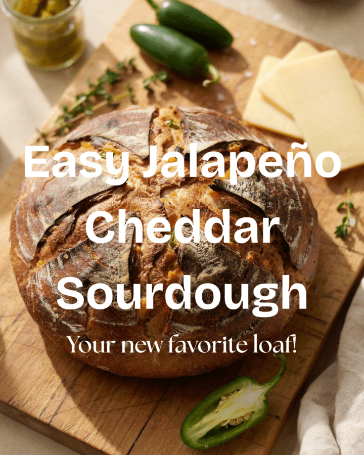 A rustic, golden-brown round loaf of jalapeño cheddar sourdough sitting on a wooden cutting board, with a few slices of creamy cheddar and fresh/pickled jalapeño peppers scattered around it. The crust is deeply browned and artisan-looking, with a beautiful scored design across the top. Warm, natural kitchen lighting and a cozy homemade-baking aesthetic.